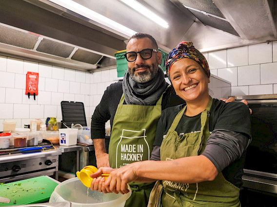 Sareta Puri and Sami Tamimi smiling at the camera wearing green Made in Hackney aprons